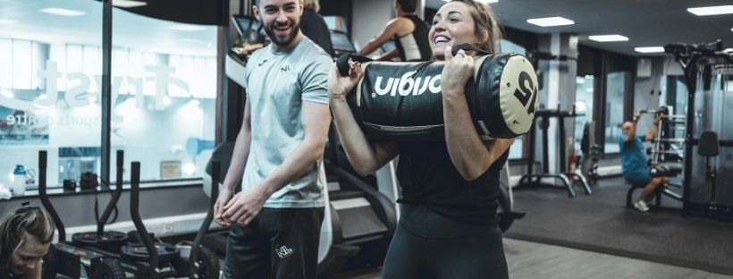 girl holding sandbag weight with personal trainer