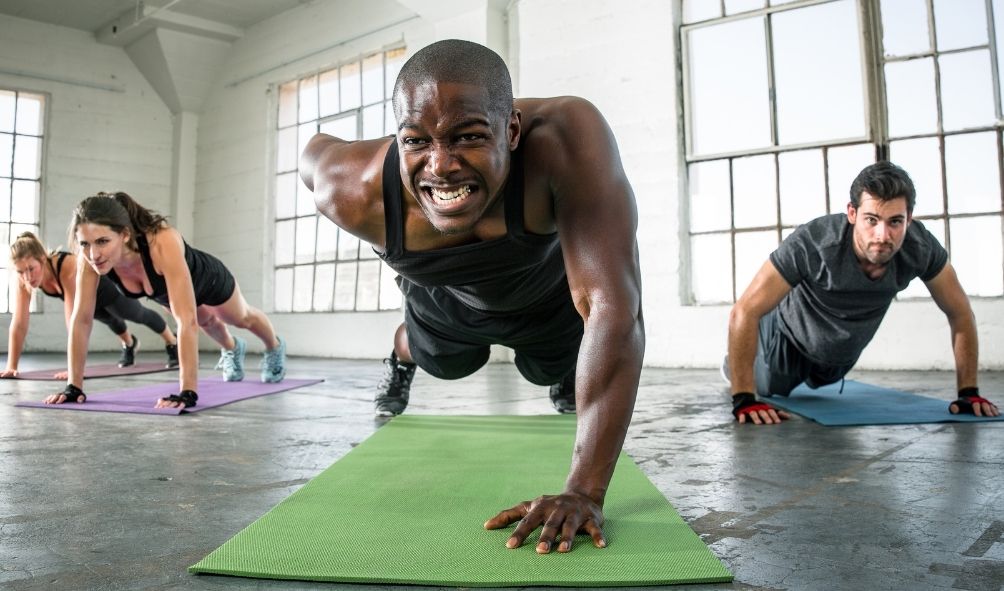 4 people doing press ups on mats on the floor of a gym or studio